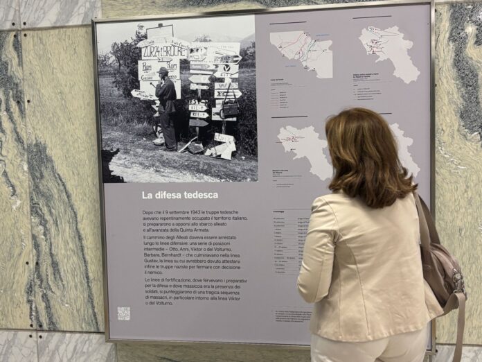 Pannello della mostra permanente sulla guerra e la liberazione di Napoli nella stazione Quattro Giornate della metro con una persona che osserva i contenuti storici esposti.