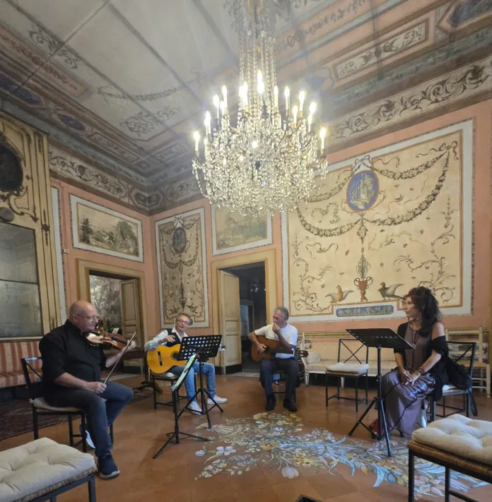 Quattro persone suonano strumenti a corda in una sala con pareti e soffitto decorati.