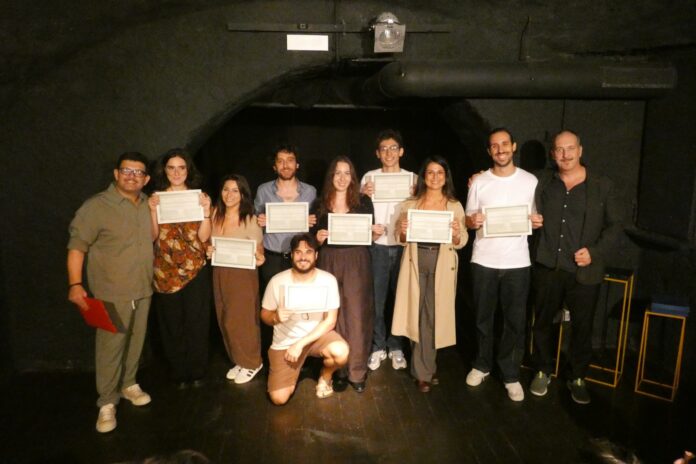 Gruppo di persone che mostrano certificati di premiazione, in un teatro.
