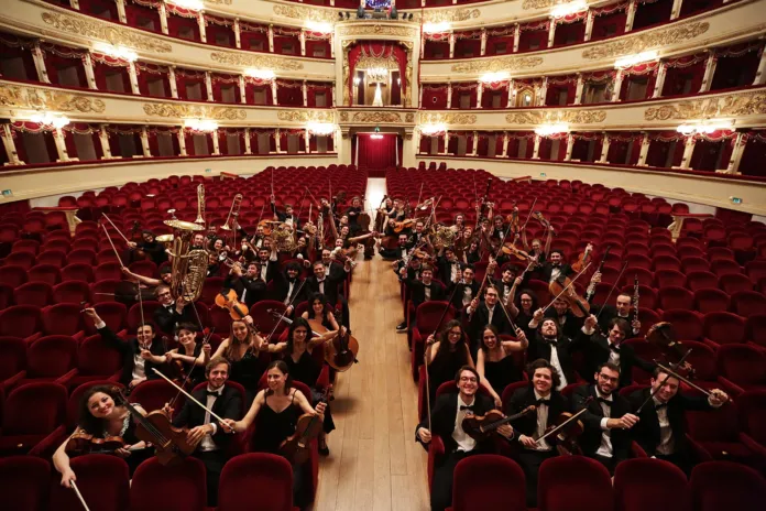 Immagine di un concerto in teatro con orchestra di giovani musicisti sul palco e pubblico in sala, foto di archivio.