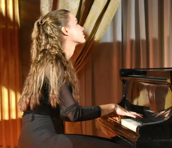 Una donna seduta al pianoforte mentre suona.