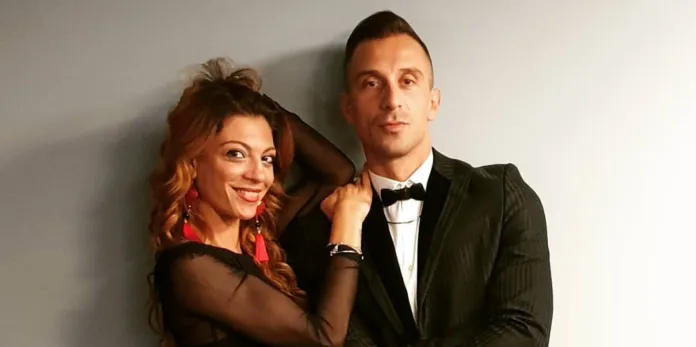 Due persone sorridenti, un uomo e una donna, posano insieme in abbigliamento elegante.