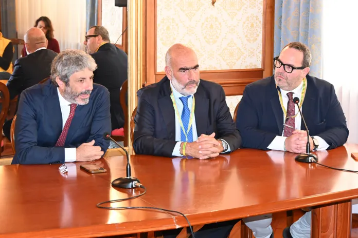 Immagine di archivio di un evento ufficiale con partecipanti seduti e un tavolo al centro.