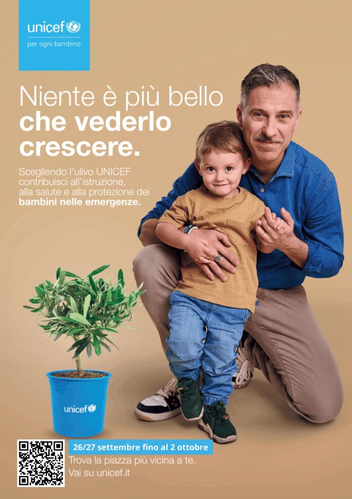 Gabriele Corsi con un bambino in una immagine promozionale della campagna UNICEF con ulivo in vaso blu con logo UNICEF.