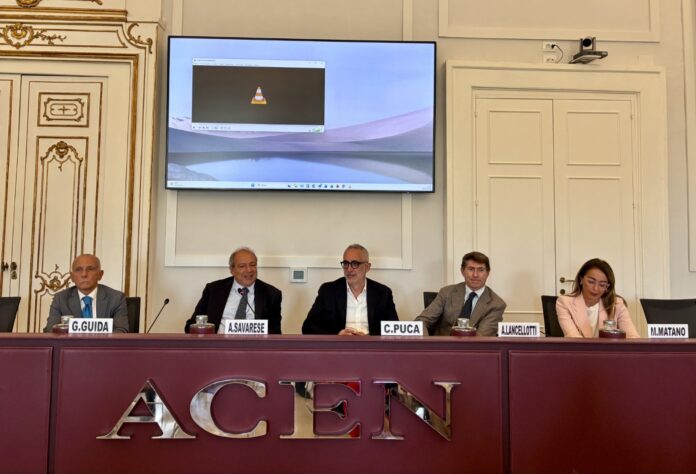 Persone sedute a un tavolo con il logo ACEN sul davanti, durante una conferenza o presentazione.
