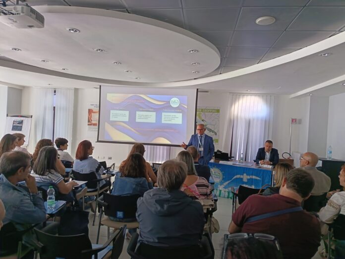 Sala conferenze con persone sedute e un relatore che parla davanti a uno schermo durante una giornata formativa.