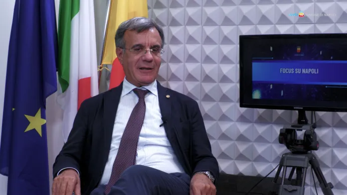 Fotografia di archivio di un assessore comunale di Napoli durante un'intervista, con bandiere sullo sfondo, in occasione di un evento pubblico.