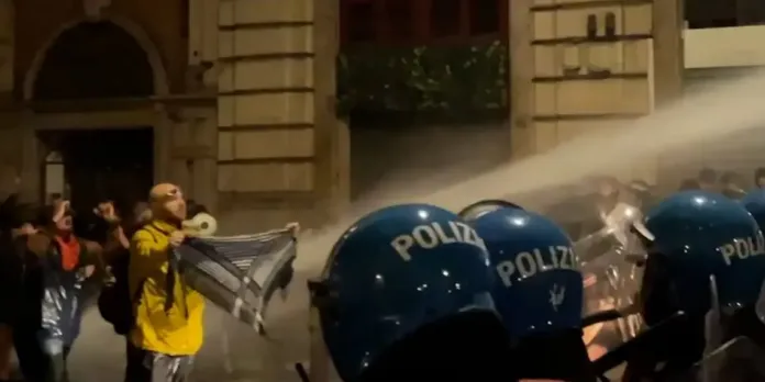 Agenti con scudi blu in primo piano e persone in strada.
