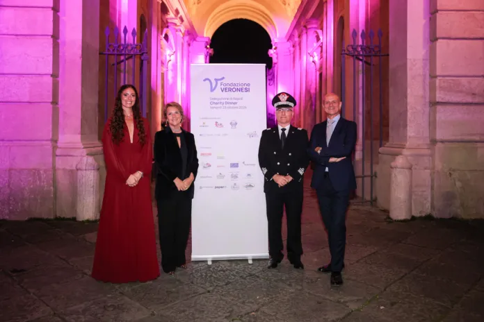 Quattro persone davanti a un pannello della Fondazione Veronesi, in un porticato illuminato di rosa.