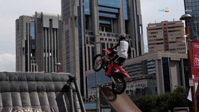 Motociclista in acrobazia su una rampa durante il Napoli Overdrive Festival al Centro Direzionale di Napoli, con edifici moderni sullo sfondo.