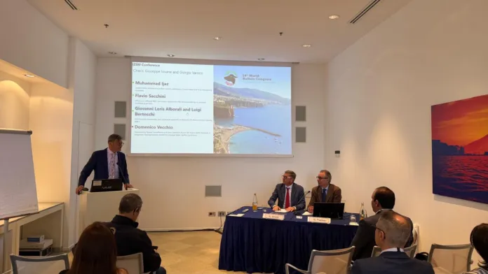 Sala conferenze con persone sedute e una presentazione proiettata sullo schermo.