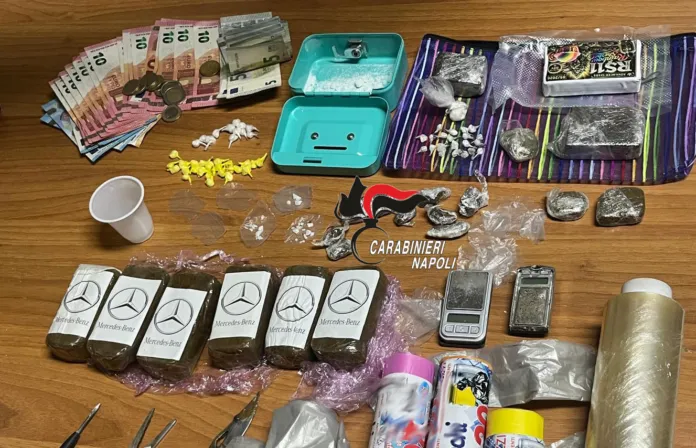 Su un tavolo sono disposti banconote, confezioni e piccoli oggetti; al centro si vede la scritta Carabinieri Napoli.