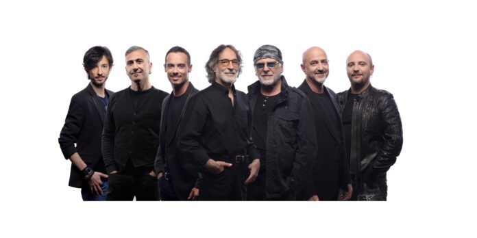 Foto di gruppo della band PFM - Premiata Forneria Marconi, musicisti in piedi sorridenti su sfondo bianco.